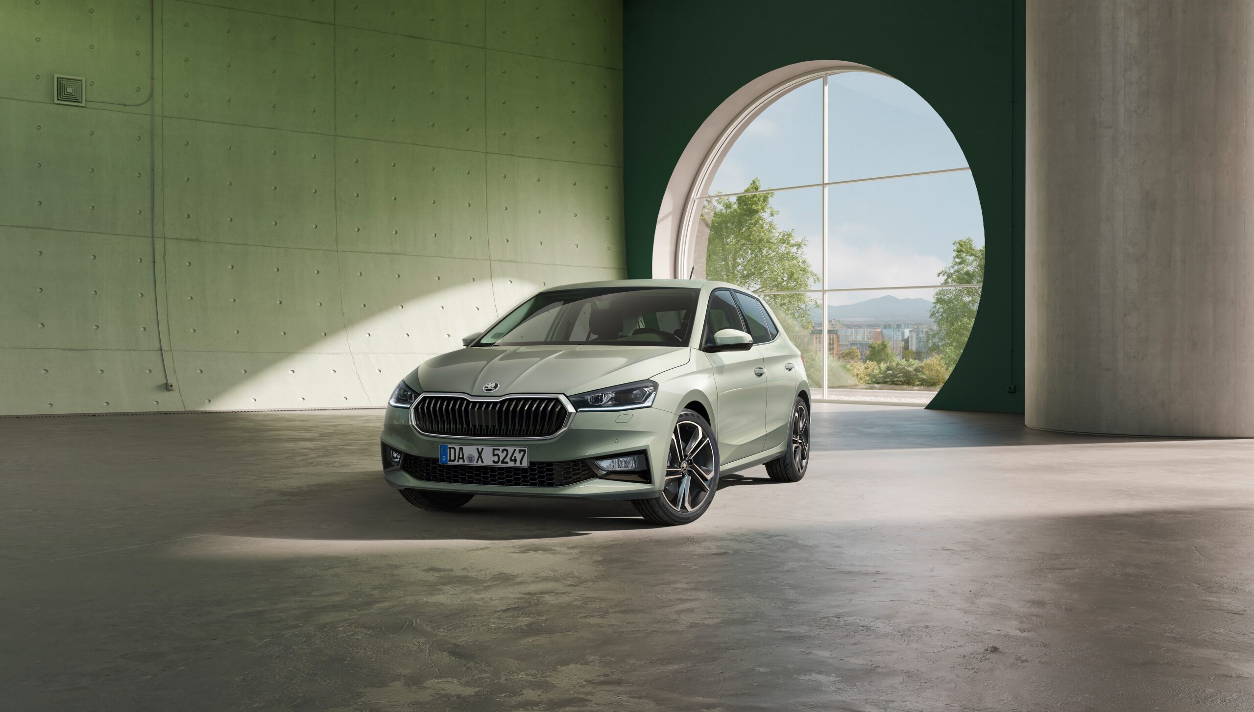 Auf dem Bild ist ein hellgrüner Skoda Fabia zu stehen. Im hintergrund ist ein großes rundes Fenster und hellgrüne Wände. Der Boden ist aus Beton.