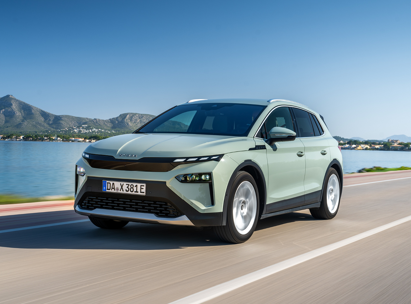 Auf dem Bild siehtt man einen Skoda Elroq, das auf der Straße fährt. Im Hintegrund sieht man Berge und einen Se.