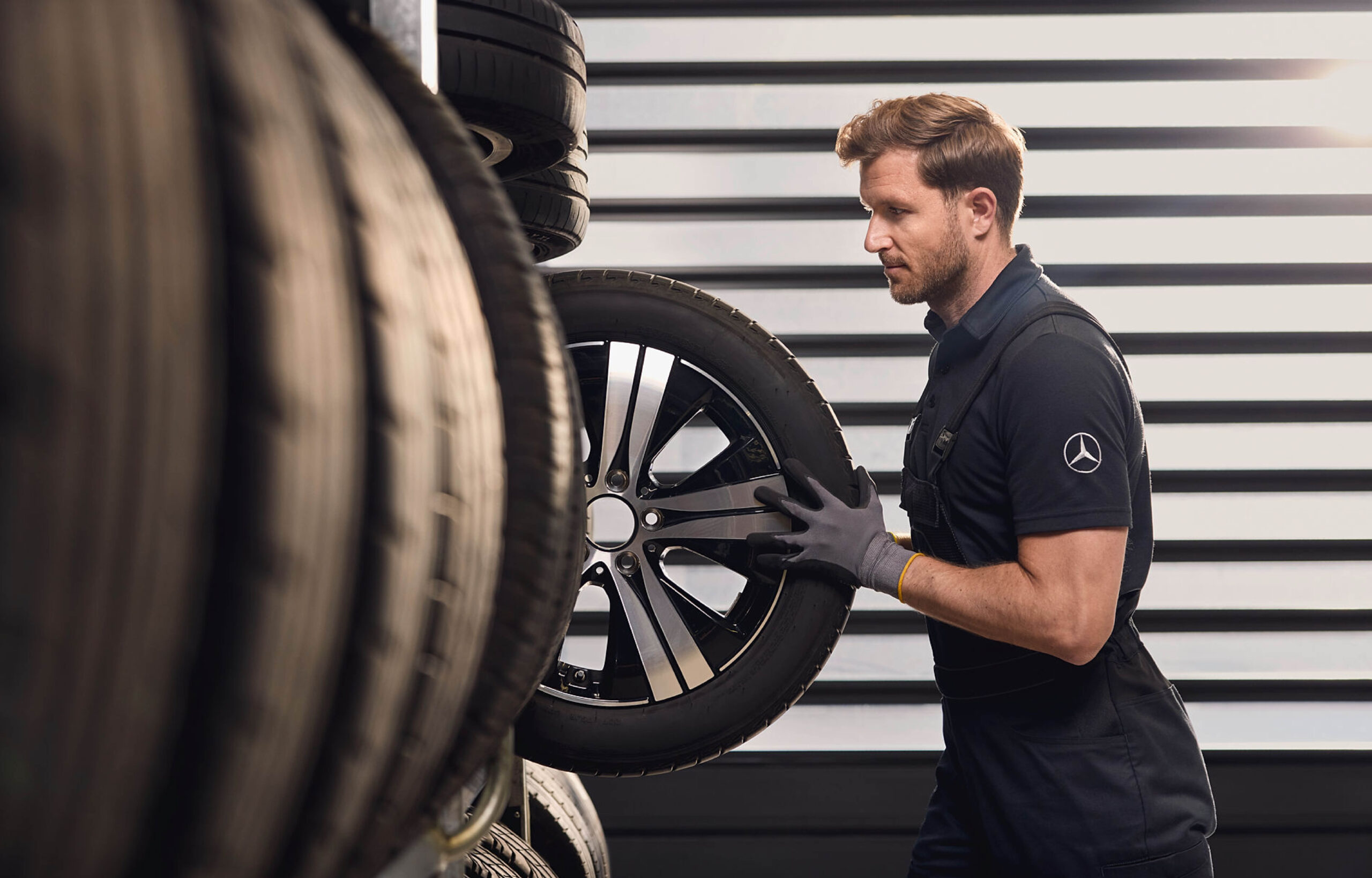 Auf dem Bild ist ein Mann mit Mercedes Montur der einen Rad aus dem Regal hebt